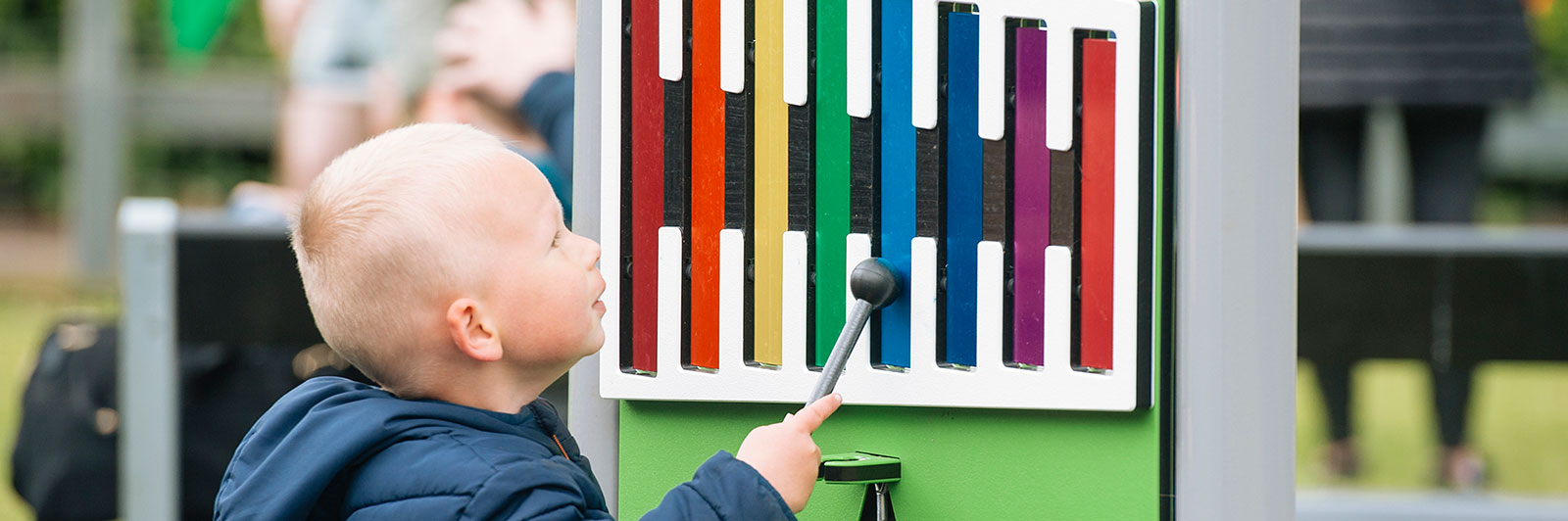 A young boy is playing with a musical play panel at a playground, it's a xylophone.